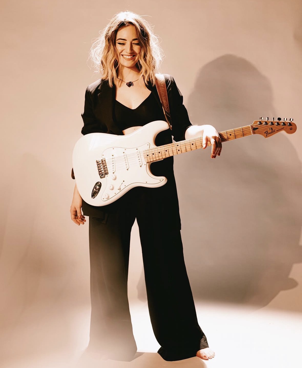 Cantora sorridente com guitarra Fender branca em ensaio