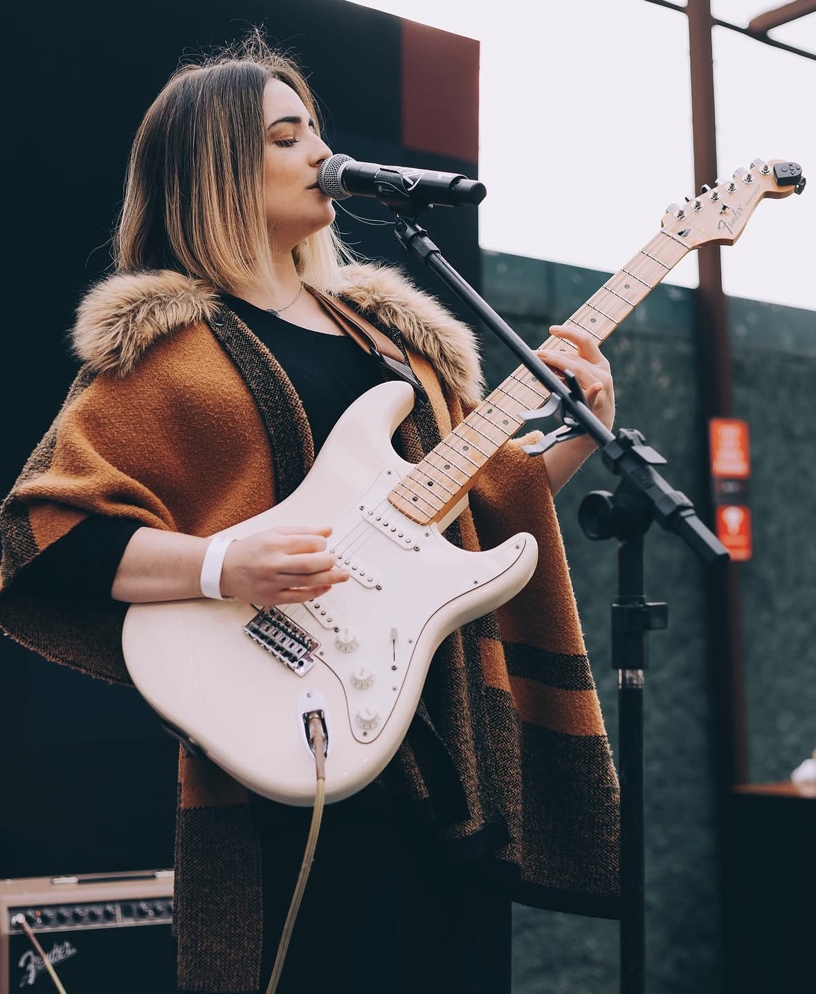 Cantora tocando guitarra e cantando ao microfone ao ar livre