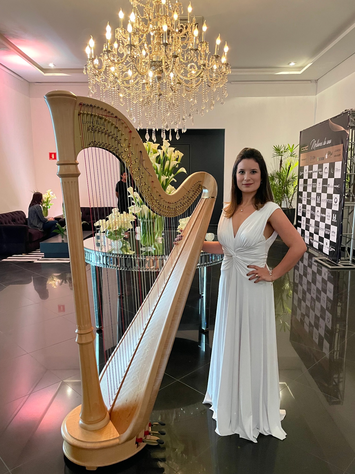 Harpista em vestido branco ao lado de harpa dourada em evento elegante